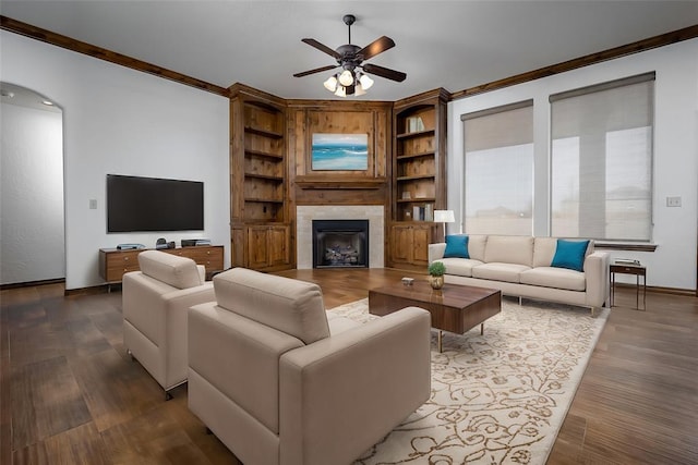 living area featuring arched walkways, a tile fireplace, wood finished floors, and crown molding