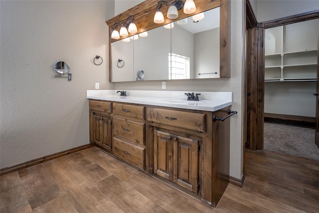 full bathroom with wood finished floors, a sink, baseboards, double vanity, and a walk in closet