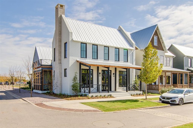 modern farmhouse style home featuring a standing seam roof, a chimney, metal roof, and covered porch