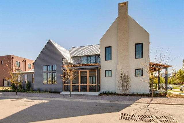 back of house with a standing seam roof, metal roof, a chimney, and a balcony