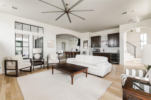 living area with arched walkways, wine cooler, light wood-type flooring, and visible vents