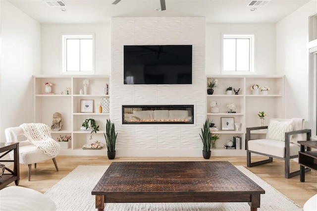 living area featuring light wood-type flooring, a tiled fireplace, and a wealth of natural light