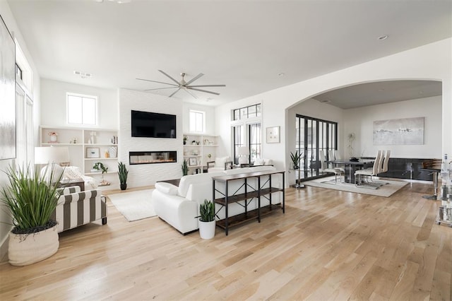 living area with arched walkways, visible vents, a fireplace, and light wood finished floors