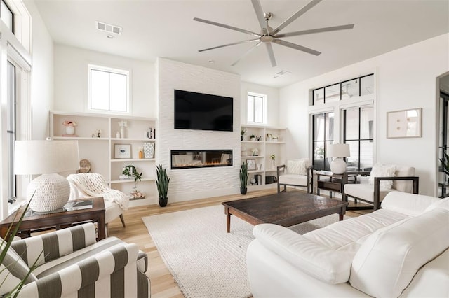 living area with light wood-style floors, visible vents, a fireplace, and a ceiling fan