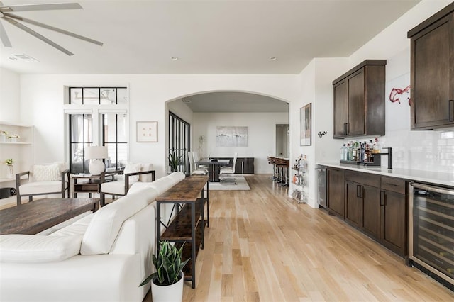 living room featuring light wood finished floors, beverage cooler, arched walkways, a ceiling fan, and a bar