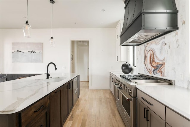 kitchen with light stone counters, a sink, hanging light fixtures, double oven range, and range hood