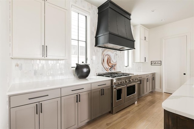 kitchen featuring light wood-style flooring, white cabinetry, double oven range, tasteful backsplash, and custom range hood