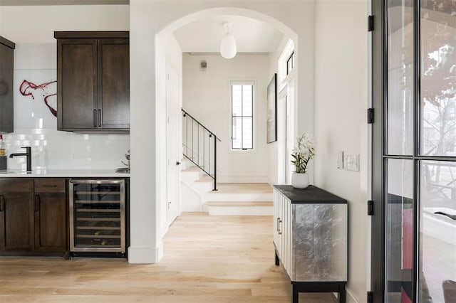 bar featuring wine cooler, arched walkways, backsplash, stairway, and light wood-style floors