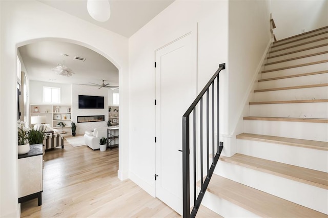 stairway featuring arched walkways, ceiling fan, a large fireplace, wood finished floors, and visible vents