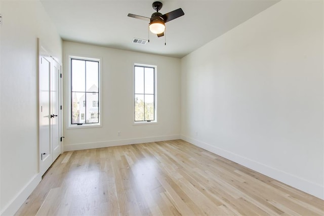 empty room with light wood-style flooring, a ceiling fan, visible vents, and baseboards