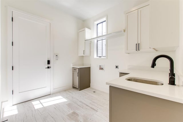 clothes washing area featuring light wood-style flooring, hookup for an electric dryer, washer hookup, a sink, and cabinet space