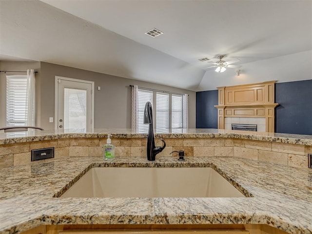 kitchen with ceiling fan, lofted ceiling, sink, and a tile fireplace