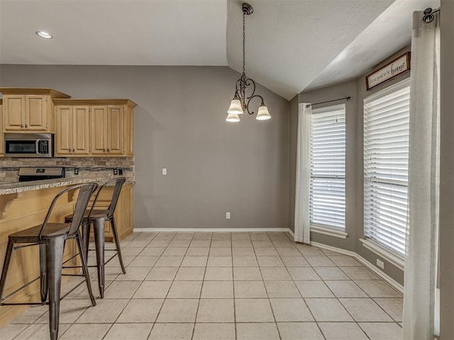 kitchen with light stone counters, a kitchen bar, decorative backsplash, vaulted ceiling, and light brown cabinets