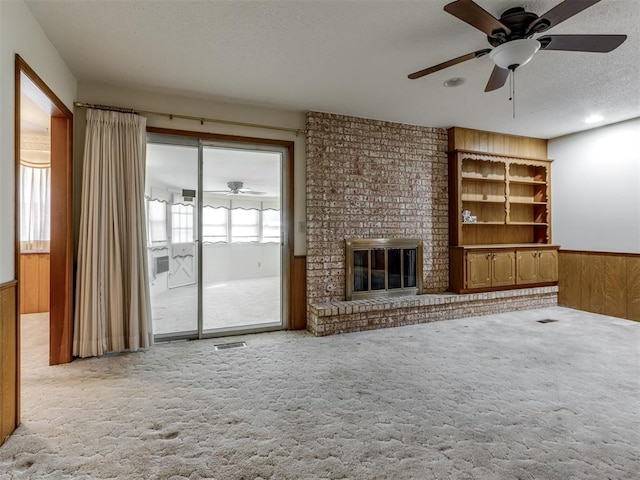 7000 N Libby Ave, Oklahoma City, OK 73132 - unfurnished living room with wood walls, carpet floors, ceiling fan, a brick fireplace, and a textured ceiling