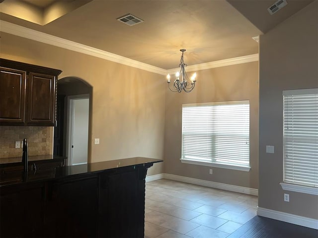 kitchen with a notable chandelier, decorative light fixtures, crown molding, dark brown cabinetry, and tasteful backsplash