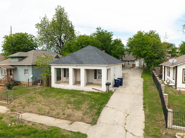 1315 NW 7th St, Oklahoma City, OK 73106 - view of front of home featuring a front lawn, fence, covered porch, roof with shingles, and driveway
