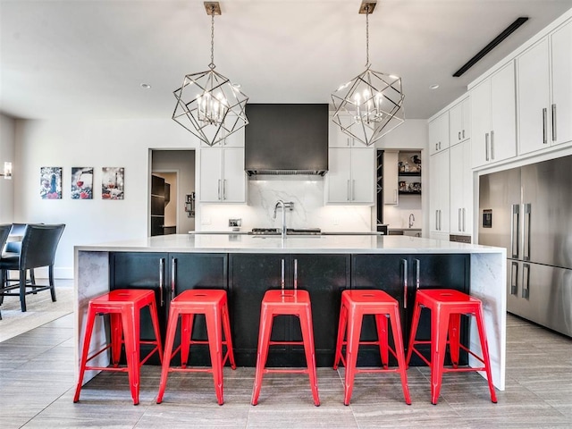 kitchen featuring white cabinets, decorative light fixtures, a large island with sink, and built in refrigerator