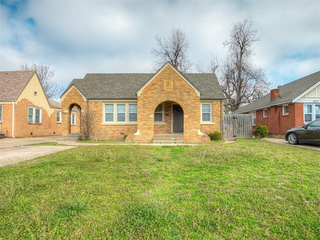 view of front facade with a front yard, fence, roof with shingles, crawl space, and brick siding