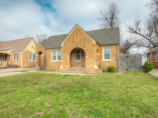 view of front facade featuring fence, brick siding, a front yard, and a shingled roof