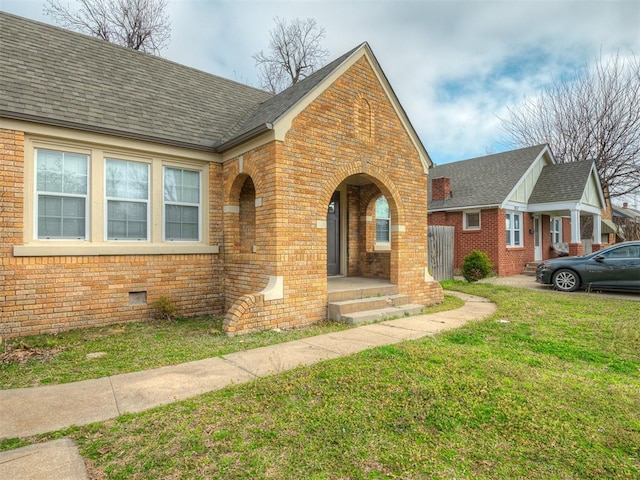 view of front of house featuring crawl space, brick siding, a front yard, and a shingled roof