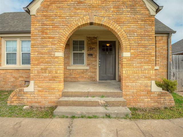 doorway to property with brick siding and roof with shingles