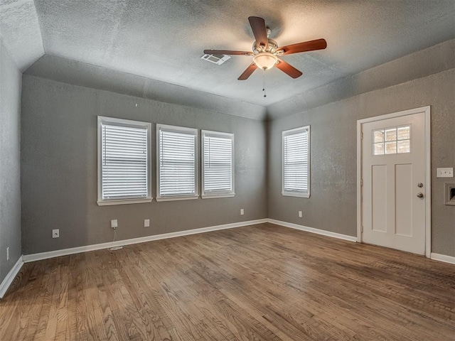 empty room featuring a ceiling fan, wood finished floors, visible vents, baseboards, and a textured ceiling