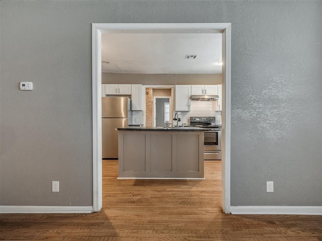 kitchen featuring light wood-style flooring, under cabinet range hood, dark countertops, white cabinetry, and stainless steel appliances