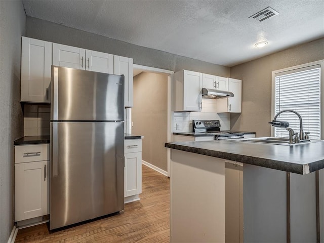 kitchen featuring under cabinet range hood, stainless steel appliances, dark countertops, and a sink