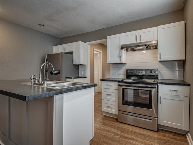 kitchen featuring under cabinet range hood, dark countertops, wood finished floors, white cabinetry, and appliances with stainless steel finishes