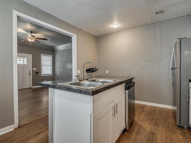 kitchen featuring dark countertops, a sink, white cabinets, stainless steel appliances, and dark wood-style flooring