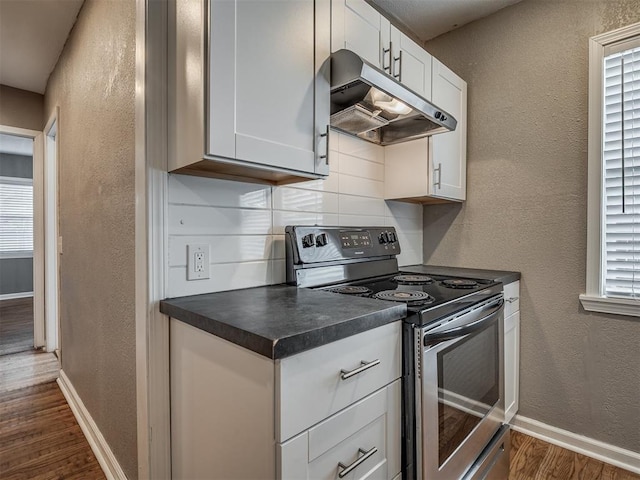 kitchen with under cabinet range hood, dark countertops, dark wood-style floors, stainless steel electric range, and a textured wall