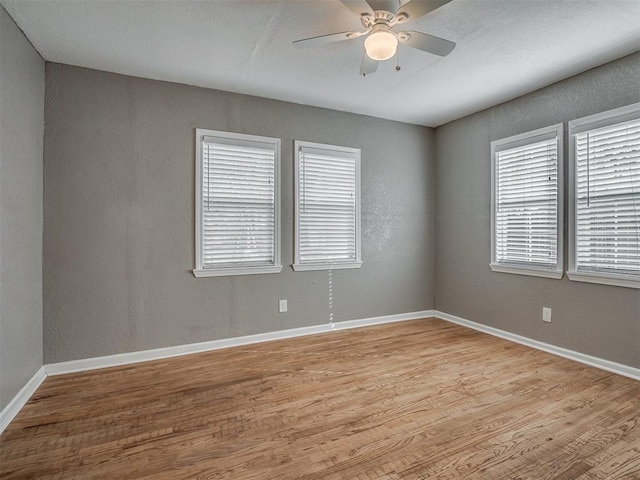 spare room with light wood-style flooring, a ceiling fan, baseboards, and a textured wall