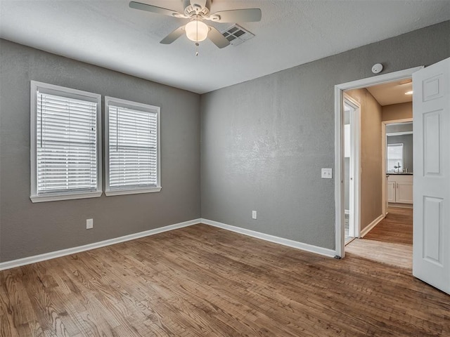 empty room with a textured wall, a ceiling fan, baseboards, and wood finished floors