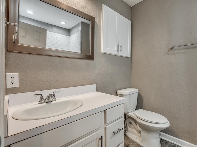 bathroom featuring baseboards, toilet, vanity, and a textured wall