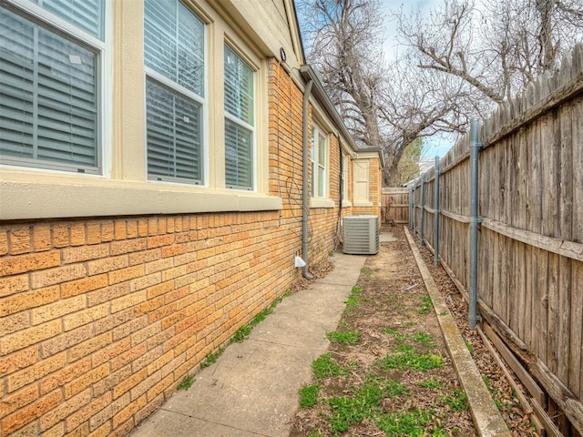 view of property exterior featuring brick siding, central AC unit, and a fenced backyard