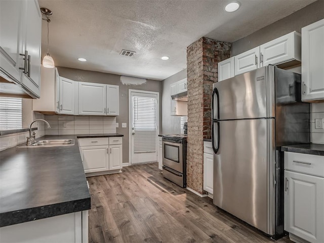 kitchen with dark countertops, light wood finished floors, white cabinets, stainless steel appliances, and a sink