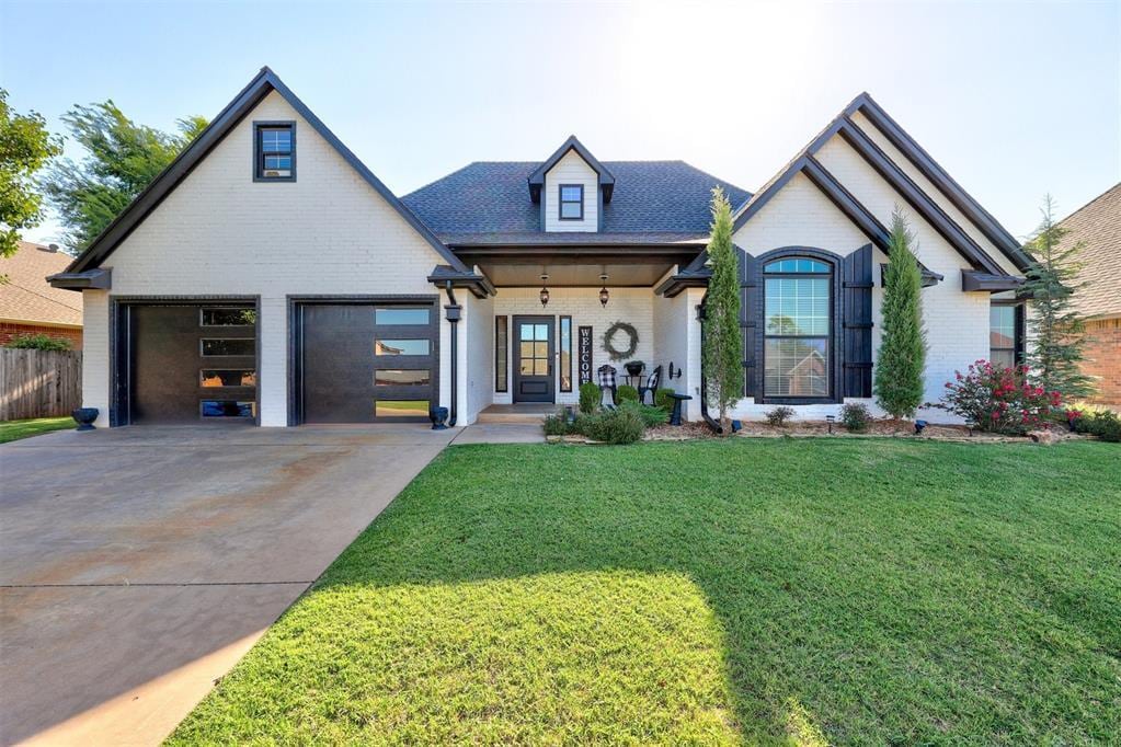 french country style house featuring a porch, a garage, and a front lawn