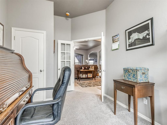 home office with light tile patterned flooring, baseboards, arched walkways, and light colored carpet