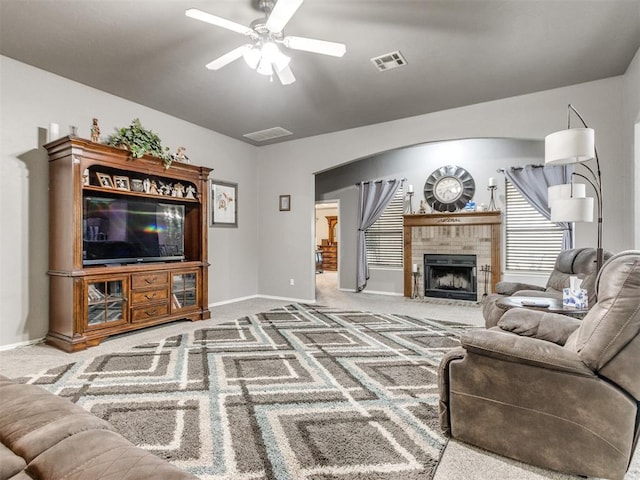 carpeted living area featuring arched walkways, a fireplace, visible vents, baseboards, and a ceiling fan