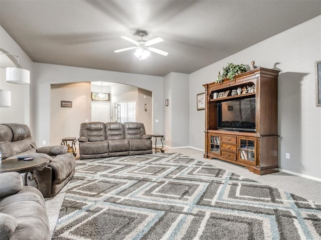 living room with arched walkways, ceiling fan, baseboards, and light colored carpet