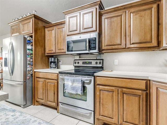 kitchen with stainless steel appliances, brown cabinetry, light tile patterned flooring, and light countertops