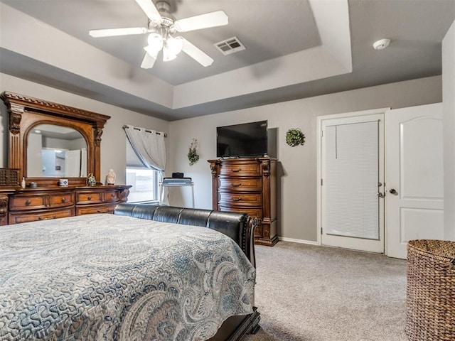 bedroom with a tray ceiling, visible vents, light carpet, ceiling fan, and baseboards