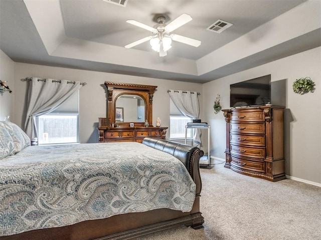 carpeted bedroom featuring visible vents, multiple windows, baseboards, and a raised ceiling