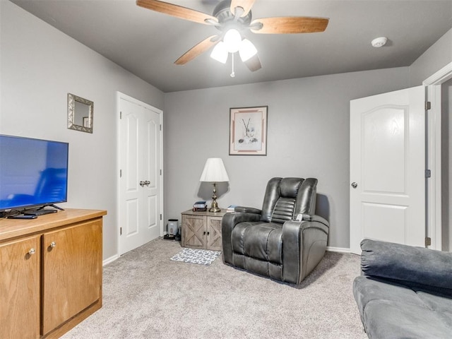 living area featuring baseboards, a ceiling fan, and light colored carpet