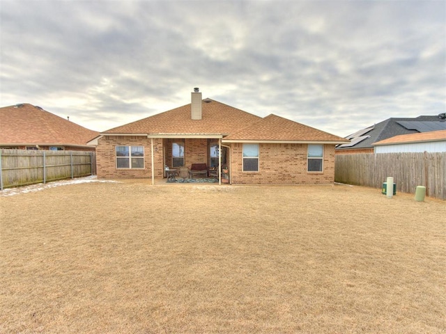 rear view of house with a patio, a fenced backyard, brick siding, roof with shingles, and a chimney