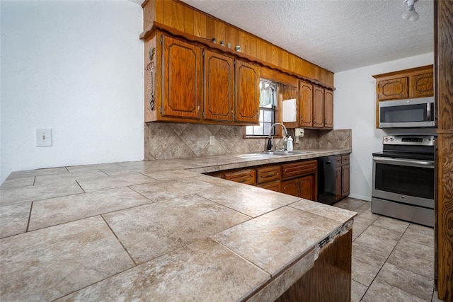 kitchen with appliances with stainless steel finishes, tile countertops, a textured ceiling, decorative backsplash, and sink