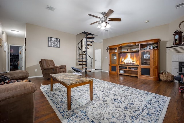 living room with a tiled fireplace, dark wood-type flooring, and ceiling fan