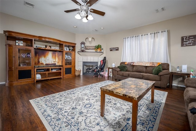 living room featuring dark wood-type flooring, ceiling fan, and a tile fireplace