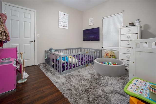 bedroom featuring a nursery area and dark hardwood / wood-style floors