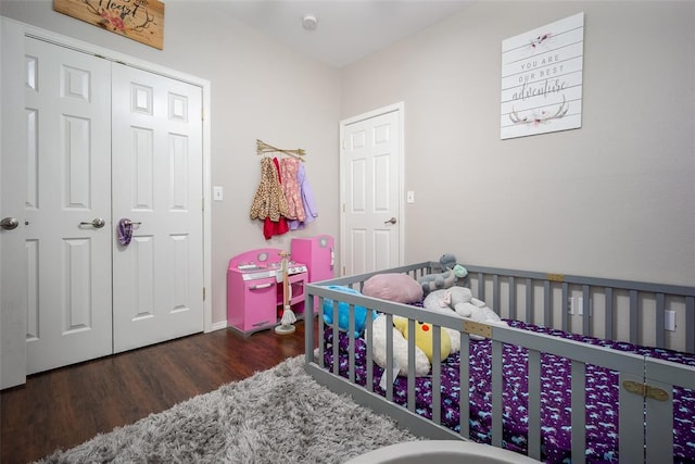 bedroom featuring a nursery area, dark wood-type flooring, and a closet